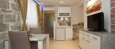 A compact kitchen with white cabinets, a built-in oven, and a flat-screen TV mounted on the wall.
