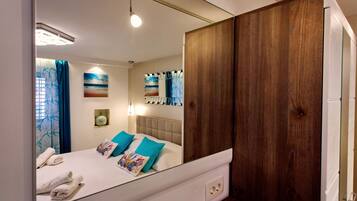 Un dormitorio con un espejo grande, una cama con ropa de cama azul y blanca, un armario de madera y obras de arte en las paredes.