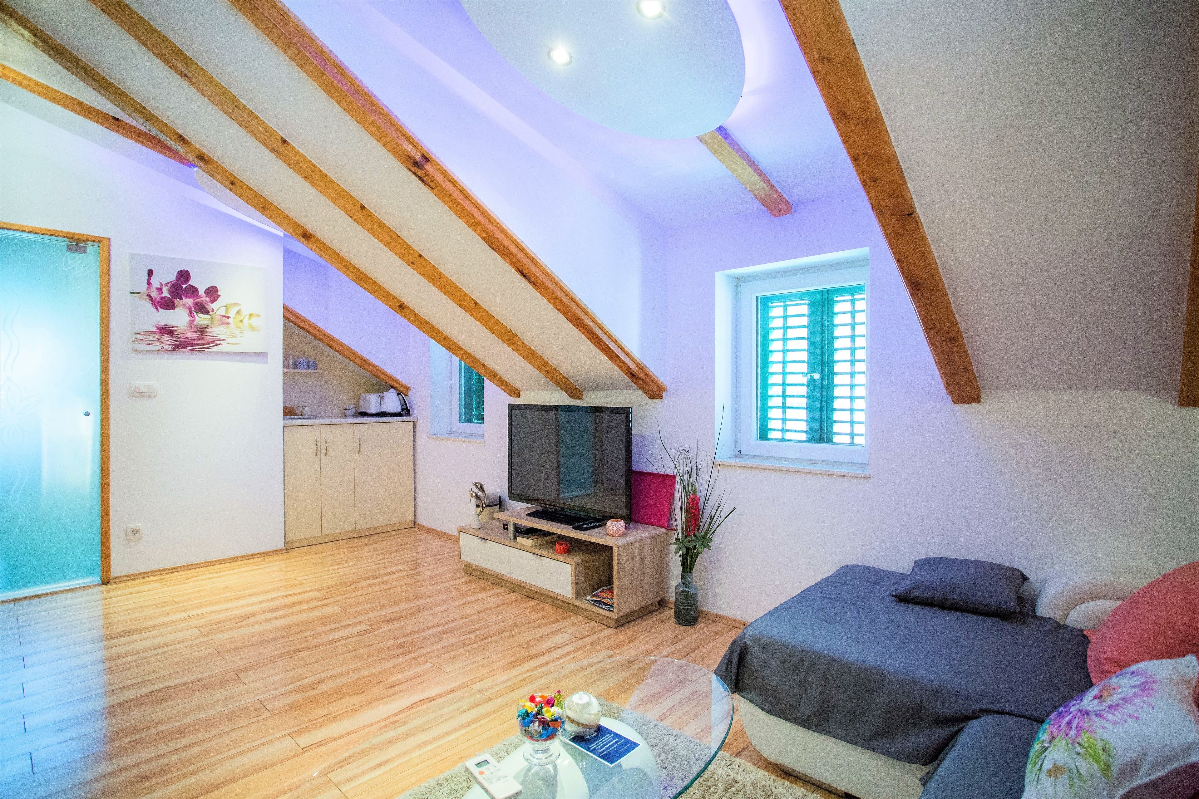 Une chambre de style loft moderne avec un plafond en pente, des poutres en bois, un grand lit, une télévision et un petit coin cuisine.