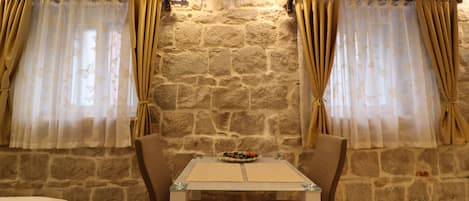 Une pièce aux murs de pierre, avec une table et des chaises, un lit et des rideaux.
