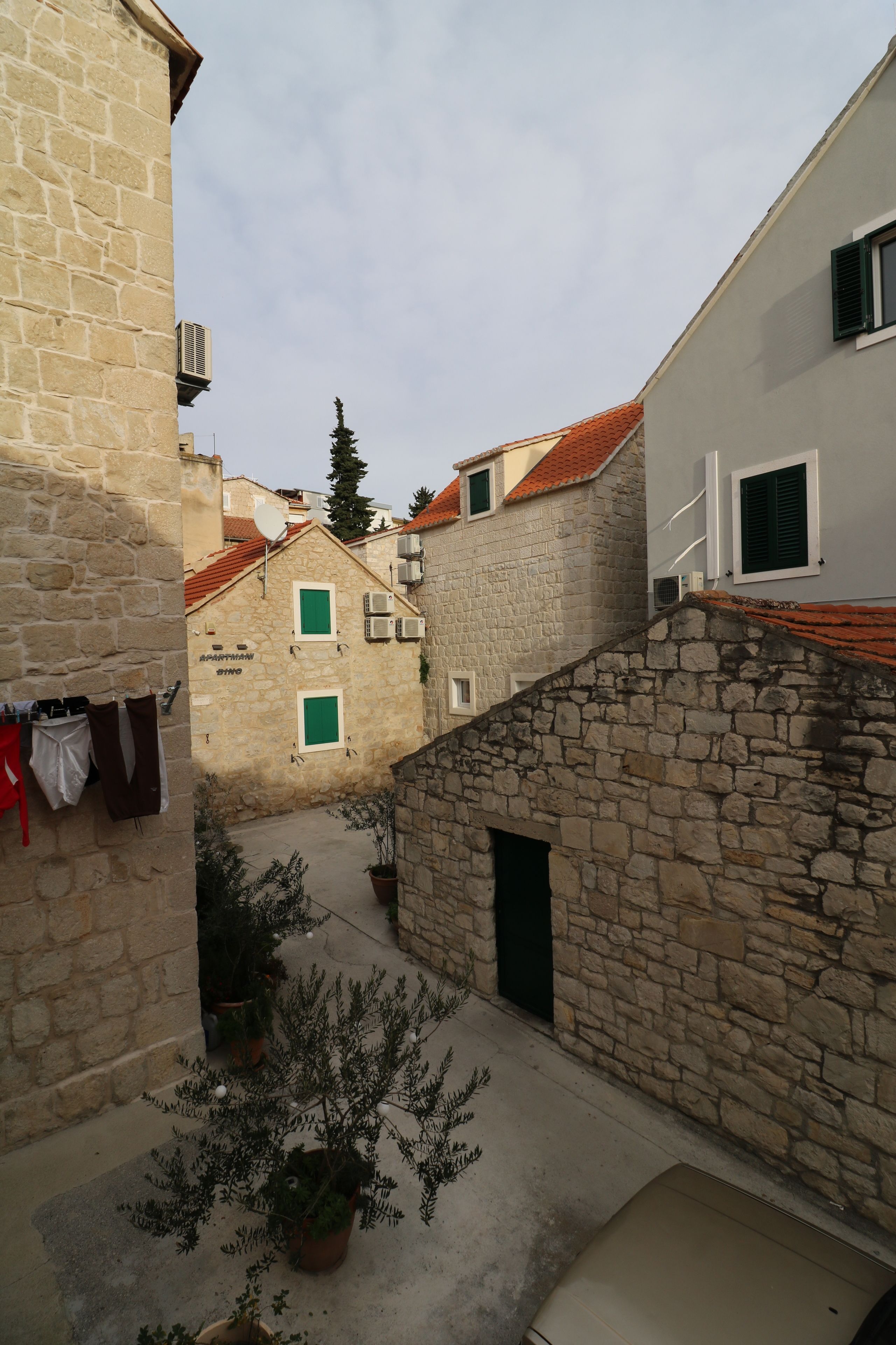 A narrow street with stone buildings, a small courtyard, and a potted plant.