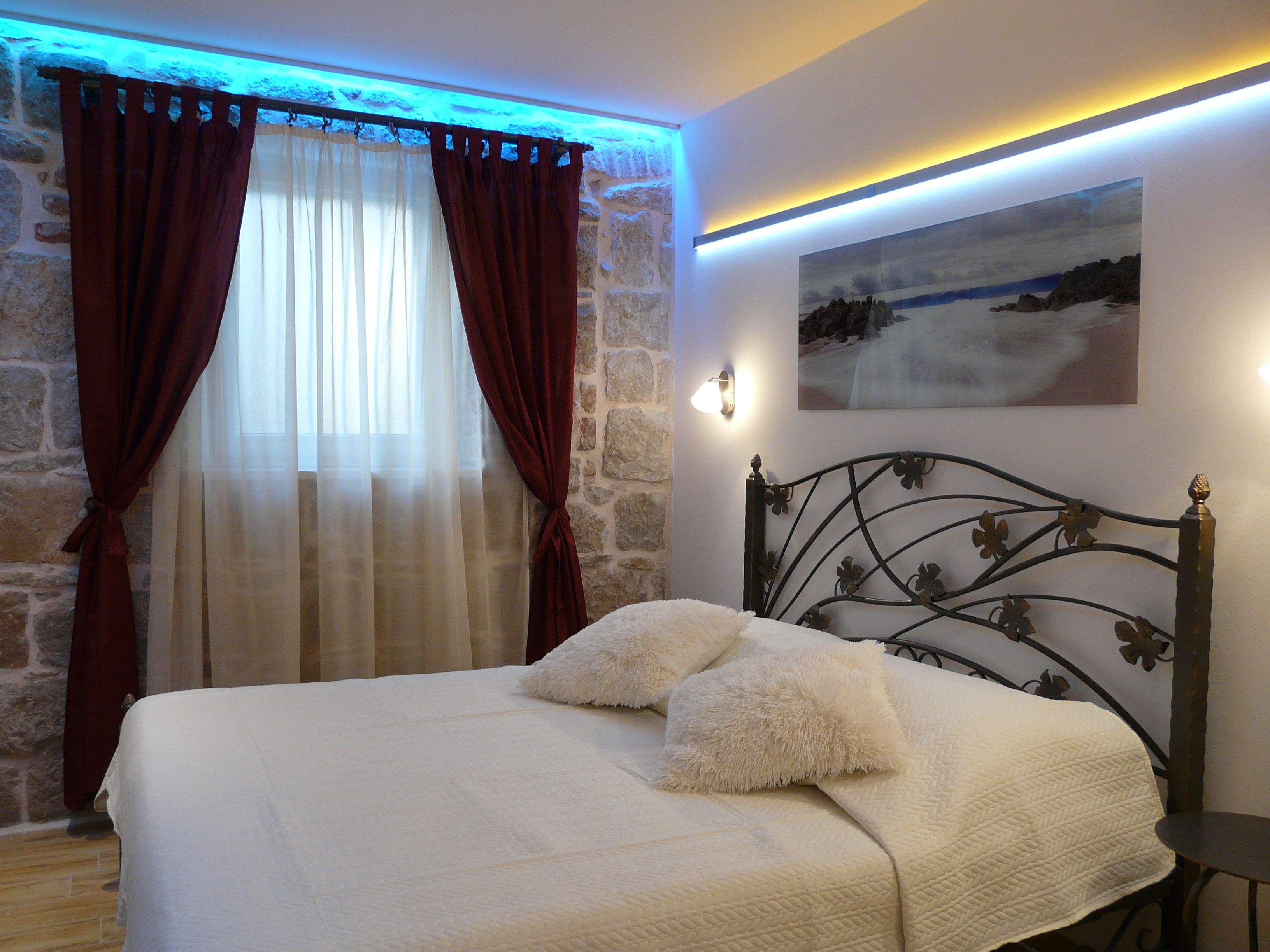 A bedroom with a stone wall, a bed with white bedding, and a painting on the wall.