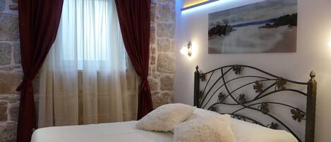 A bedroom with a stone wall, a bed with white bedding, and a painting on the wall.