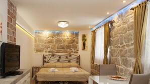 A bedroom with a stone wall, a bed with a metal headboard, a TV on a dresser, and a dining table with chairs. - House Sandra (Split)