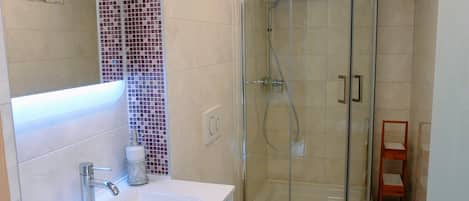 Un baño con cabina de ducha de vidrio, lavamanos blanco y un inodoro.