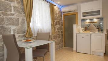Une cuisine de taille réduite avec un mur en pierre, une table en verre et un réfrigérateur blanc.