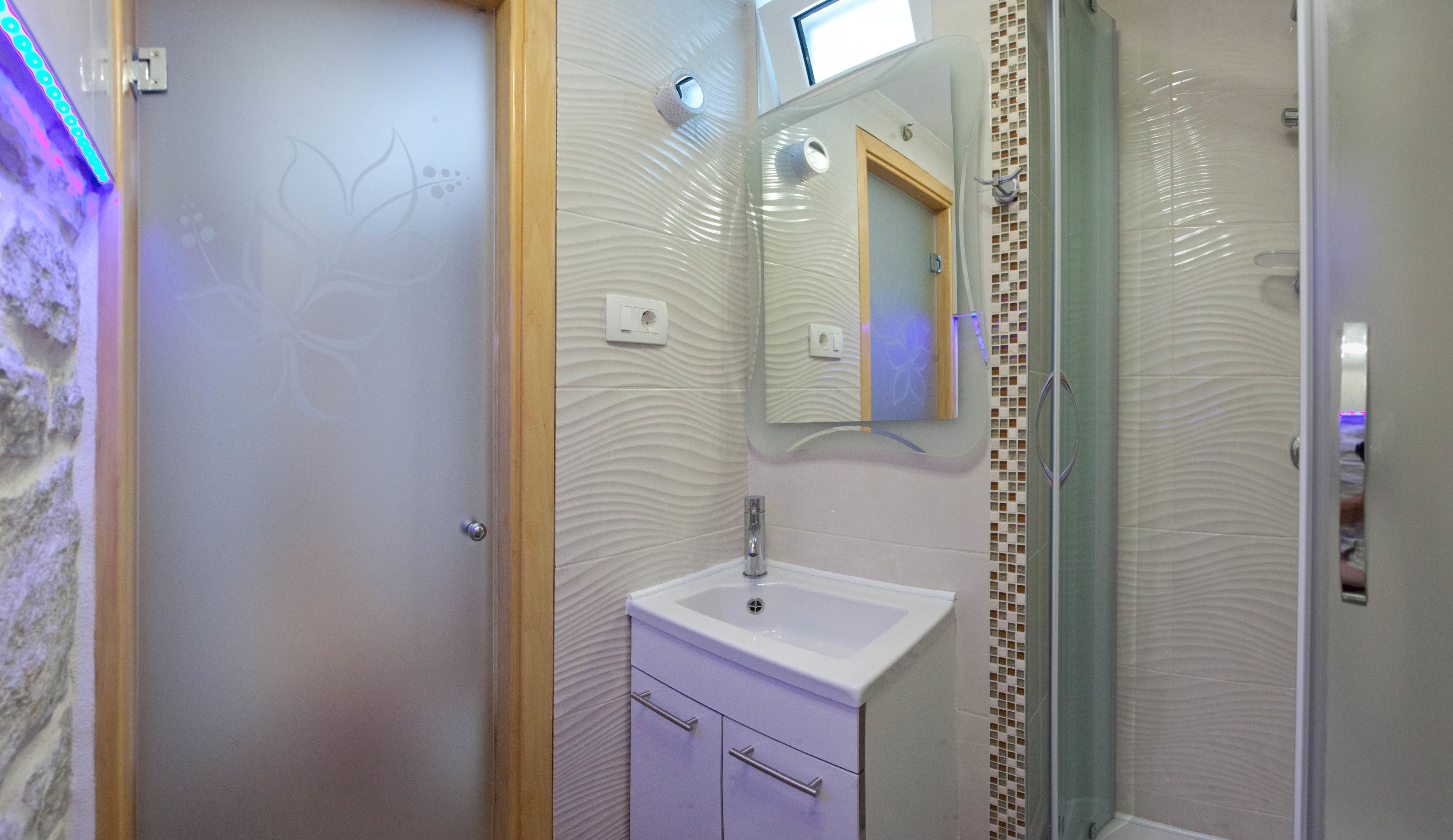 Une salle de bain avec un lavabo blanc, un miroir et un espace douche.