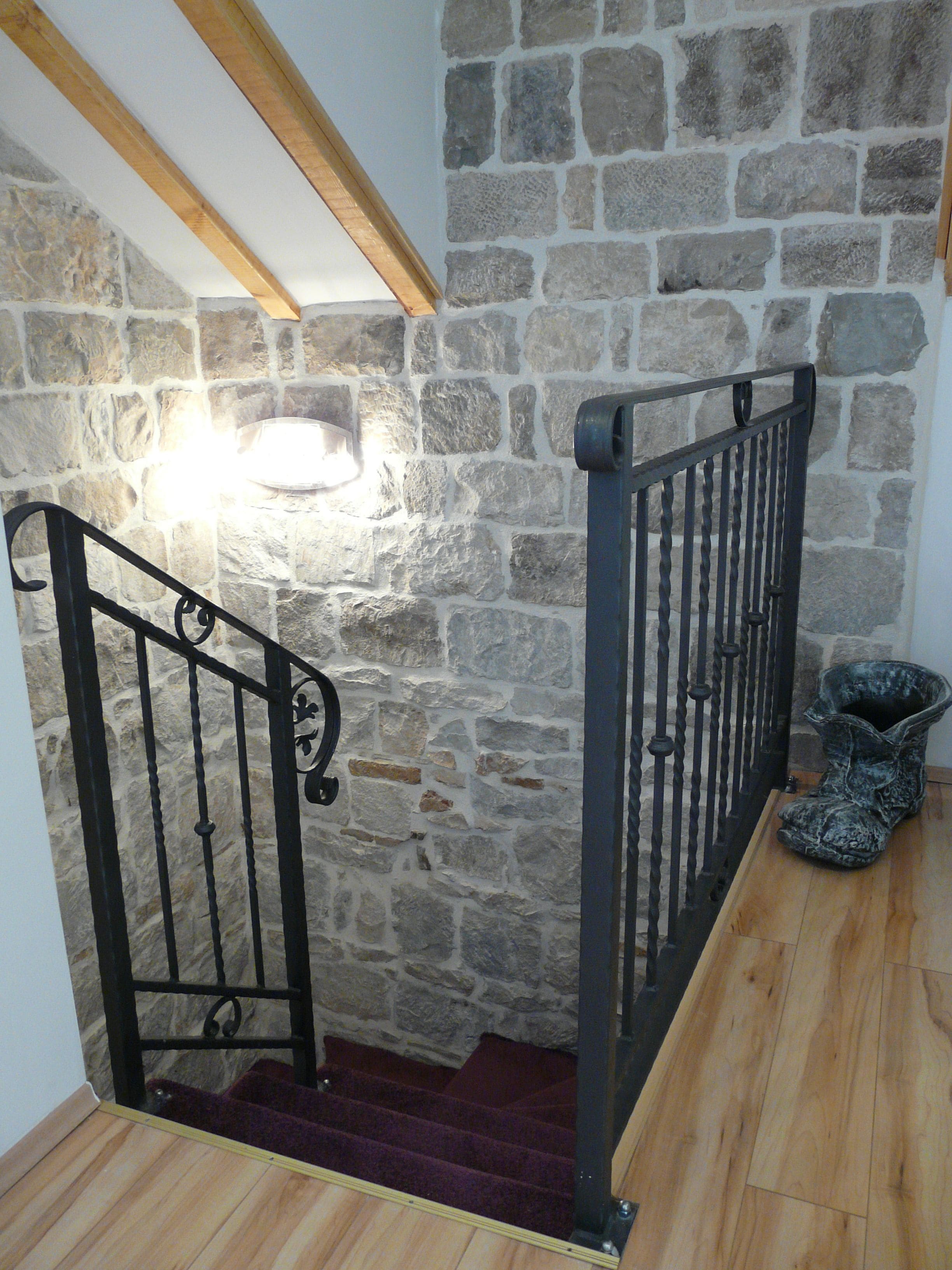 A staircase with stone walls and wooden beams, leading to a landing with a light fixture.