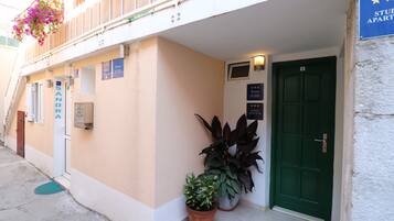Un immeuble avec une porte verte, une enseigne indiquant « APPARTEMENTS-STUDIOS » et plusieurs plantes en pot.