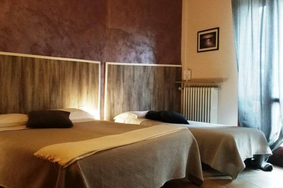 Una habitación de hotel con dos camas, cabecero de madera, mesita de noche con lámpara y radiador.