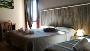 A hotel room with a large bed, a smaller bed, a wooden headboard, a nightstand with a lamp, and a framed picture on the wall.