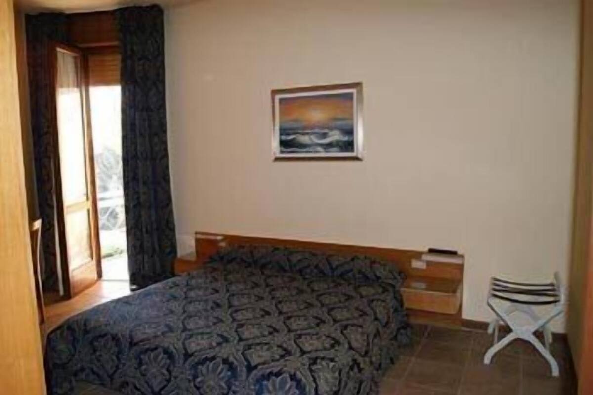 Un dormitorio con una cama, una mesita, una silla y un cuadro en la pared.