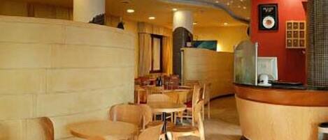A restaurant interior with round tables and chairs, a counter with a menu display, and a ceiling with recessed lighting.