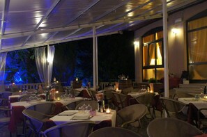 An outdoor dining area with tables set for a meal, surrounded by chairs and covered by a canopy. - Albergo Renata (Lazise)