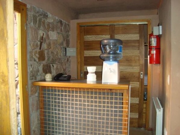 Un pasillo con pared de piedra, puerta de madera, extintor y suelo de baldosas.