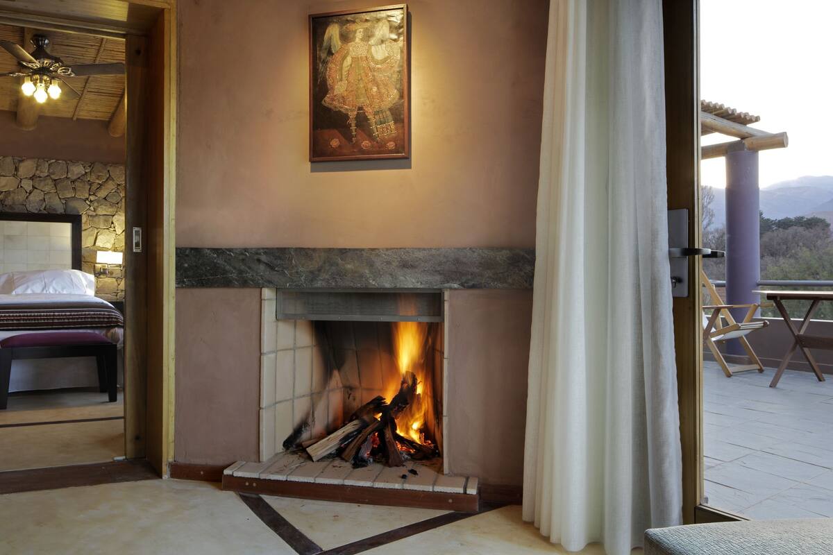 Une chambre avec un mur en pierre, une cheminée et un lit avec une banquette.