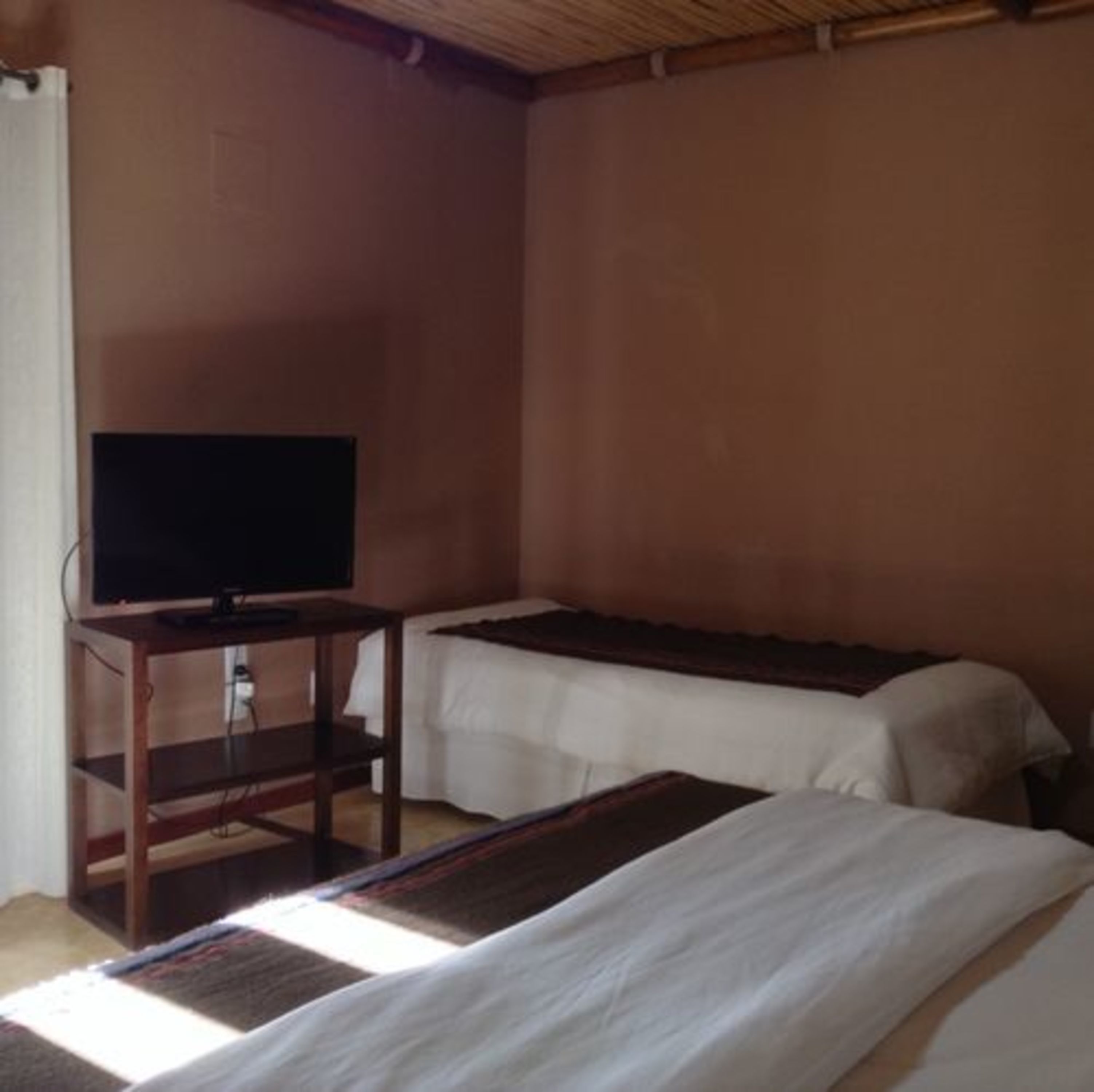A room with two beds, a television on a wooden stand, and a plain wall.