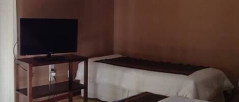 A room with two beds, a television on a wooden stand, and a plain wall.