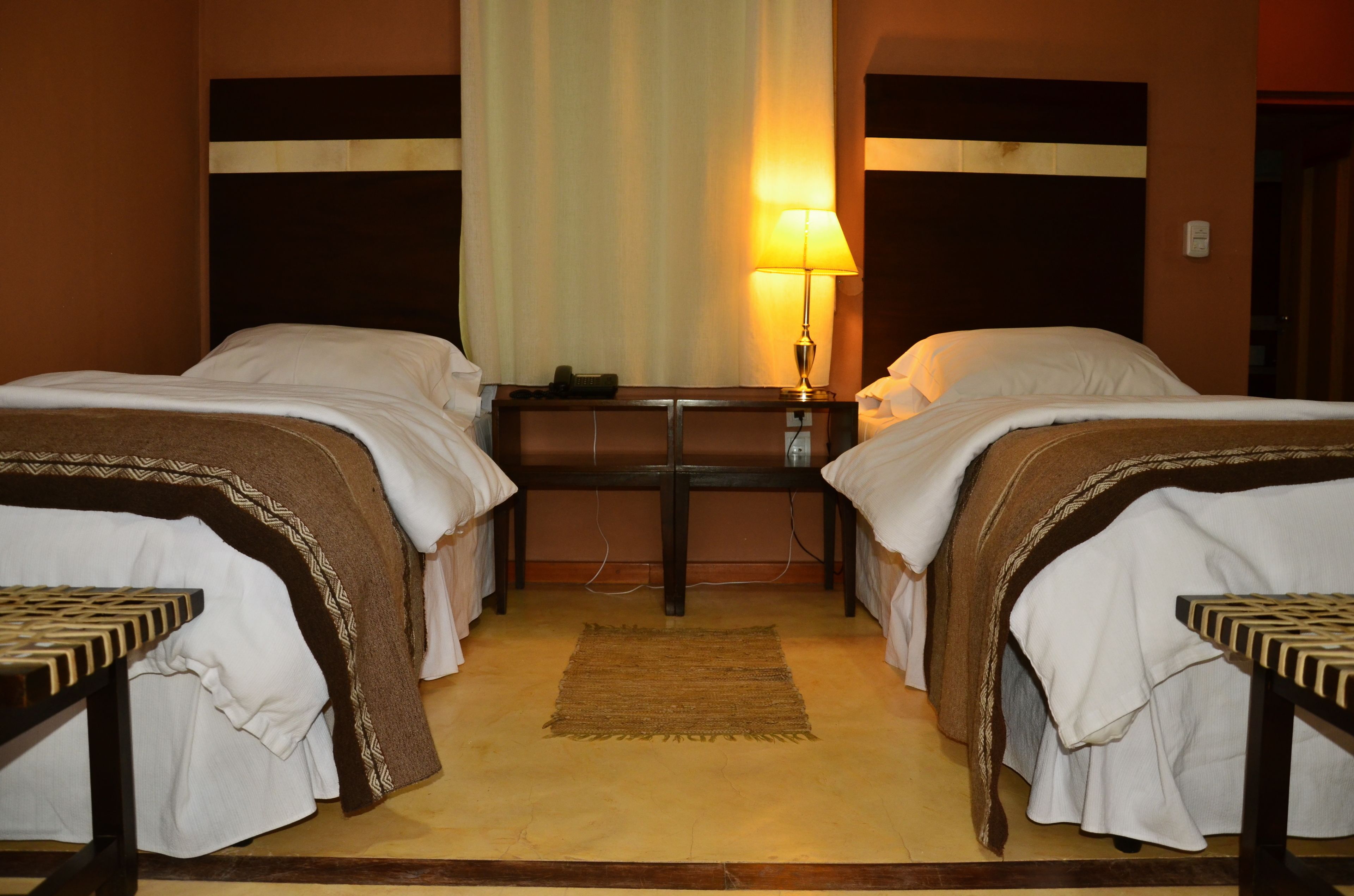 Una habitación de hotel con dos camas individuales, una mesita de noche con lámpara y una pequeña mesa.