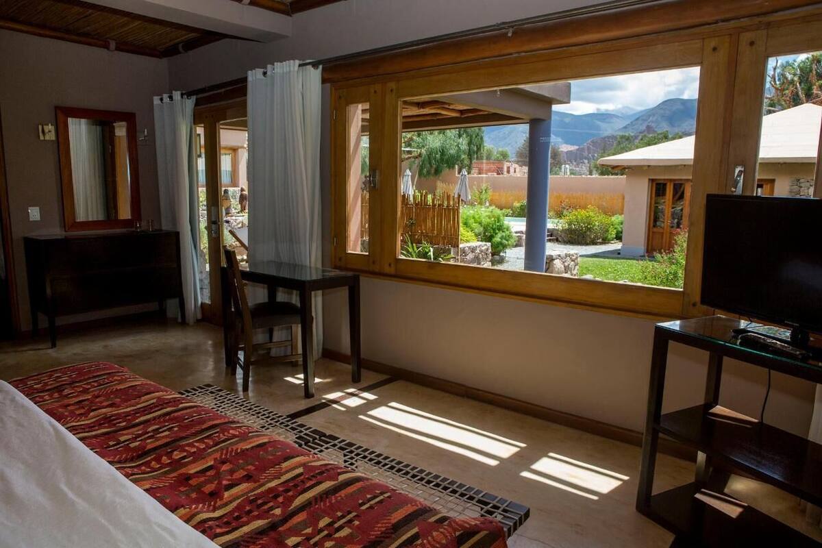 Une chambre avec un lit, un bureau, une télévision et une fenêtre donnant sur un jardin et des montagnes.