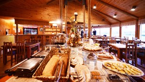 Un bufé con diversos alimentos, mesas y sillas de madera en un restaurante con decoración de madera y ventanas amplias.