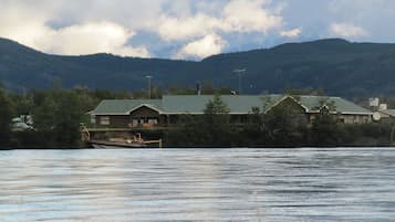 Un chalet au bord du lac, avec un bateau amarré devant, entouré de collines boisées.