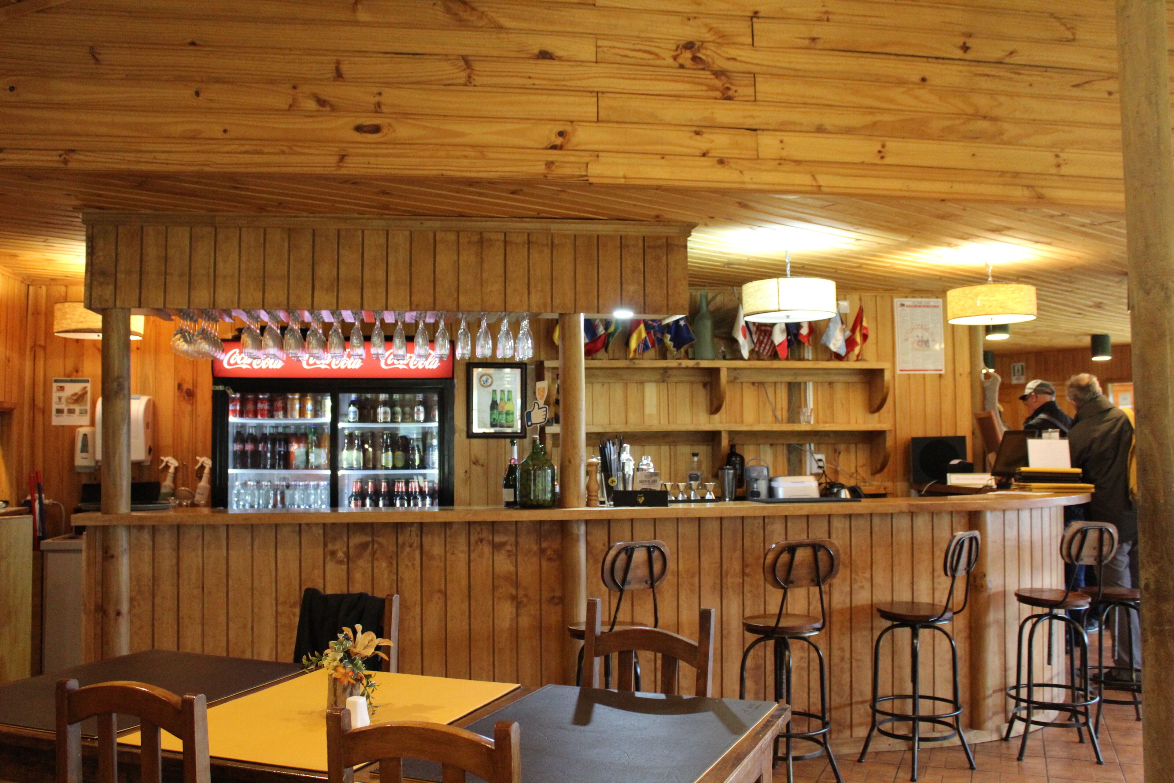 Un interior de madera con una zona de bar, sillas de madera y una mesa con un jarrón de flores.