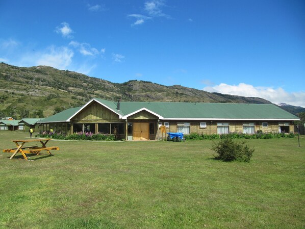 Una cabaña con techo verde, fachada de madera y una mesa de picnic al frente.