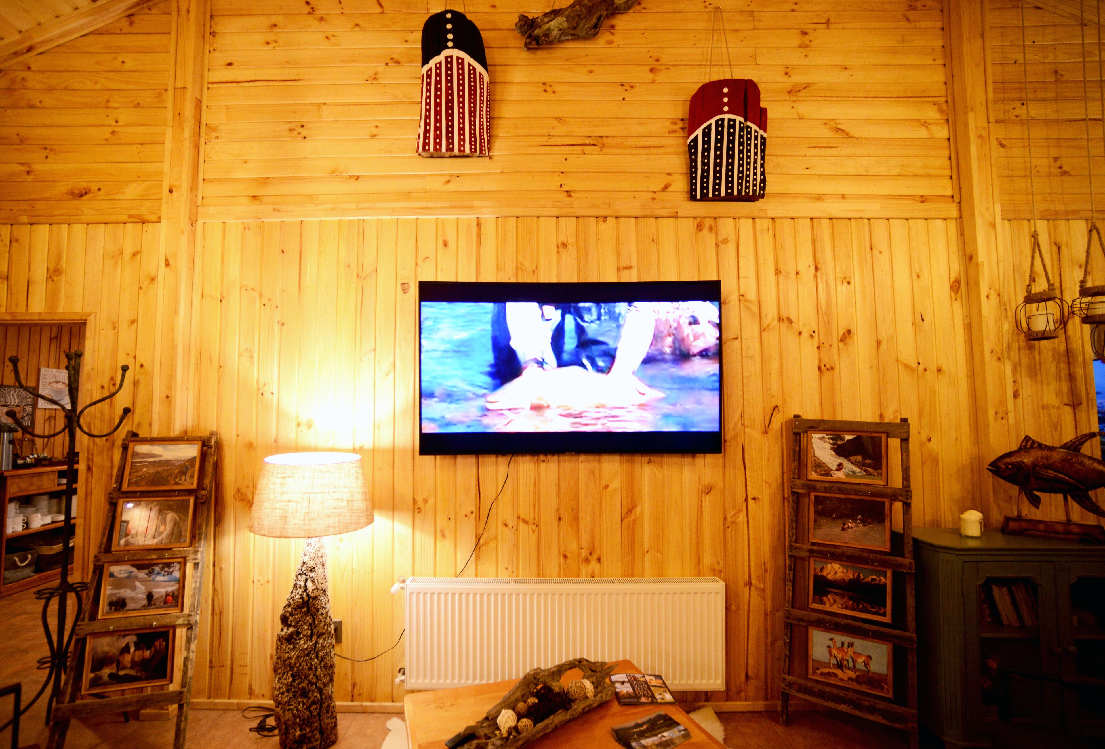 Interior de madera con un televisor montado en la pared, una lámpara y marcos de cuadros en estantes.