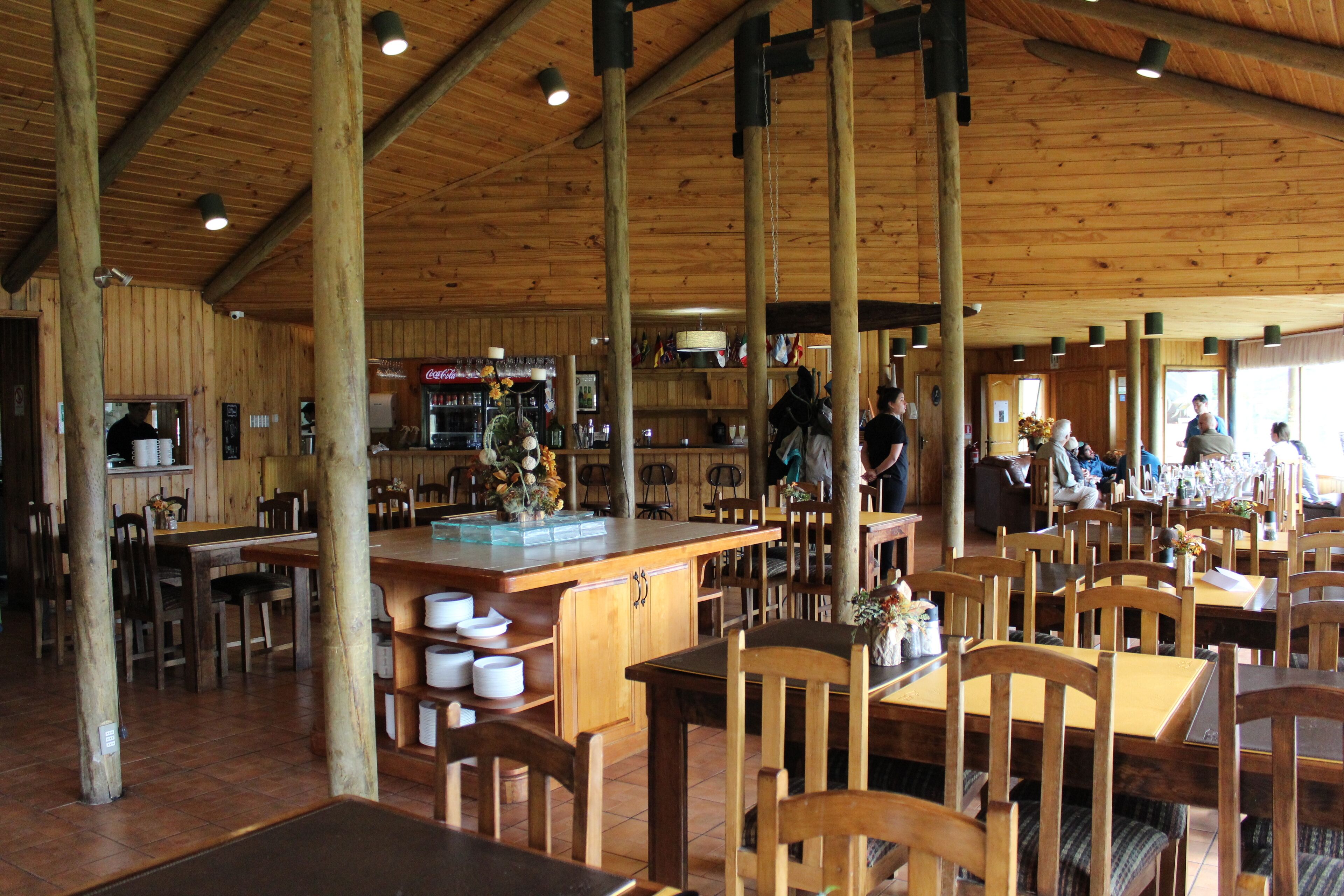 A spacious restaurant with wooden interiors, multiple dining tables, and a bar area.