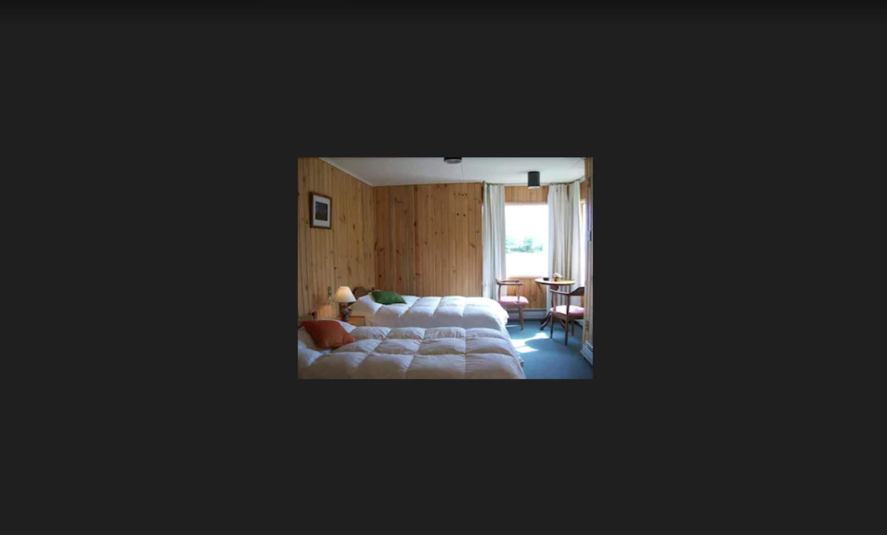 Un dormitorio con cama, una silla, una mesa y una ventana.