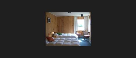 Un dormitorio con cama, una silla, una mesa y una ventana.