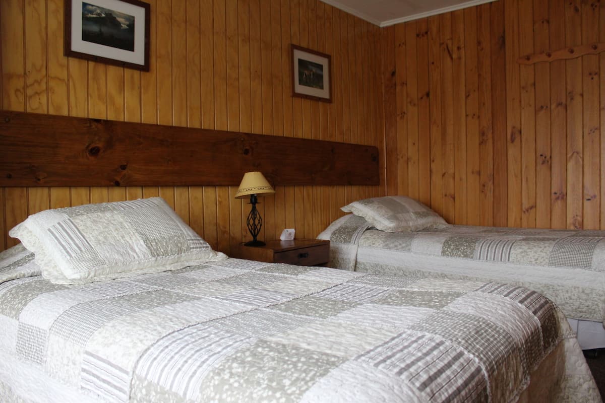 Una habitació amb dos llits, parets de fusta i una nit falda amb una làmpada.