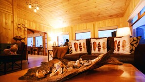 Interior acogedor de una cabaña con paredes de madera, una mesa de comedor de madera y un sofá con almohadones decorativos.