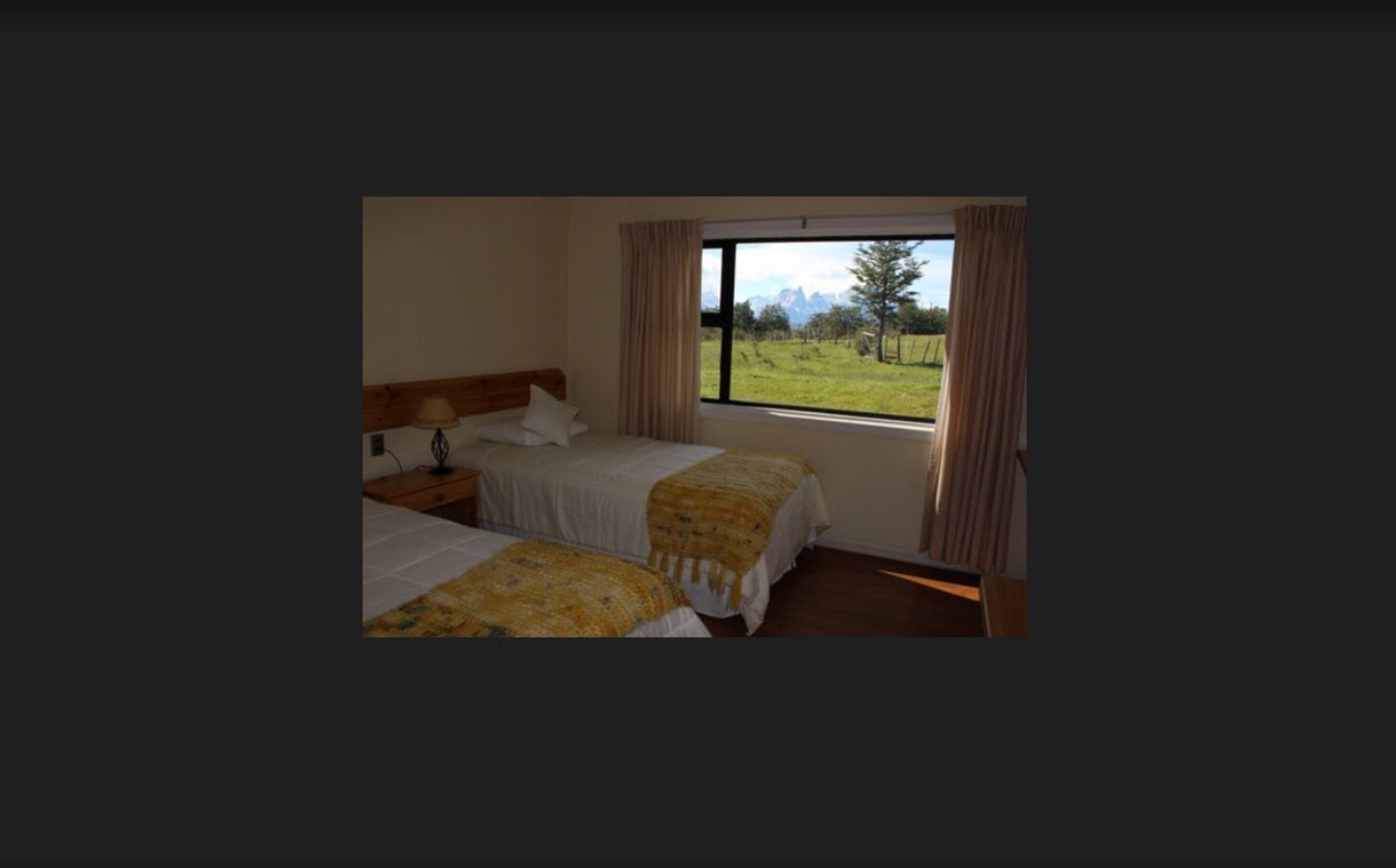 A room with two beds, a window with curtains, and a view of a grassy field.