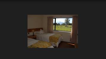A room with two beds, a window with curtains, and a view of a grassy field.