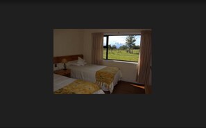 Una habitación con dos camas, una ventana con cortinas y vistas a un campo verde.