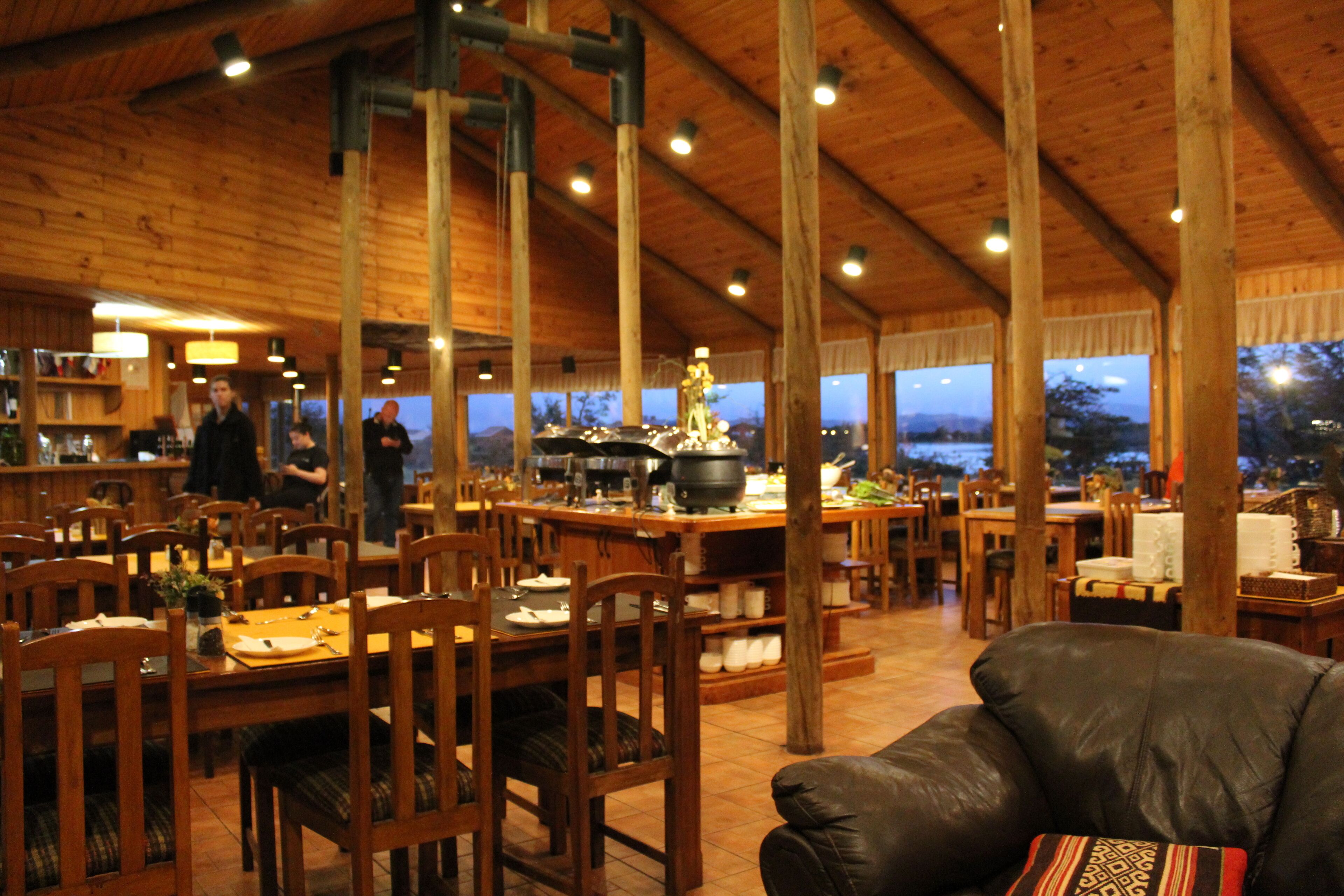A spacious dining area with wooden tables and chairs, a central island with cooking equipment, and large windows offering a view of the outdoors.