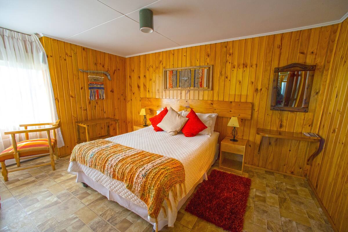 Habitació amb panells de fusta, un llit, una cadira, una tauleta de nit i un mirall.