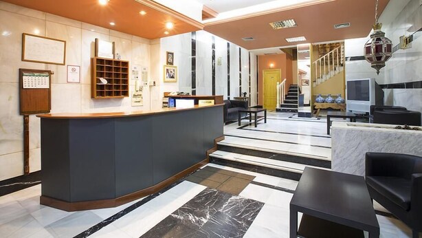 A hotel lobby with a reception desk, seating area, and a staircase leading to an upper floor. - Hostal Casa Salvador (Granada)