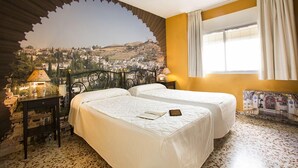 A hotel room with two beds, a view of a town through a decorative arch, a window with curtains, and a small table with a lamp. - Hostal Casa Salvador (Granada)