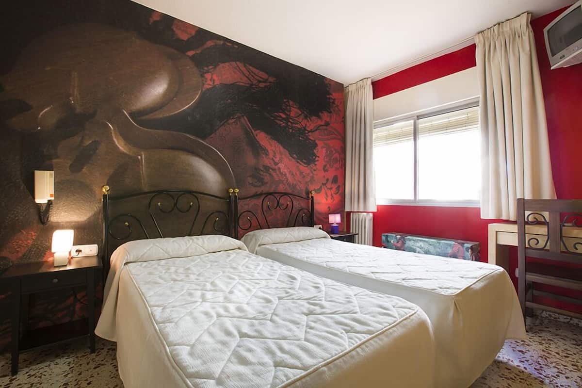 Habitación de hotel con dos camas, un mural grande en la pared, una ventana con cortinas, una mesita de noche con lámpara y una silla.