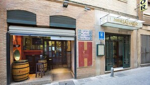 A brick building with a closed shutter on the left and a sign for 'hostal SALVADOR' on the right. - Hostal Casa Salvador (Granada)