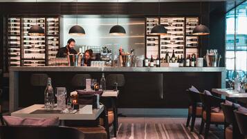 A modern bar area with a bartender, wine racks, and seating for guests.