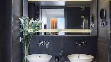 Ein modernes Badezimmer mit zwei großen weißen Waschbecken, einem großen Spiegel und dunkel gefliesten Wänden.