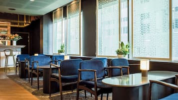Un moderno vestíbulo de hotel con zona de estar, ventanas amplias con paneles decorativos y una barra con botellas.