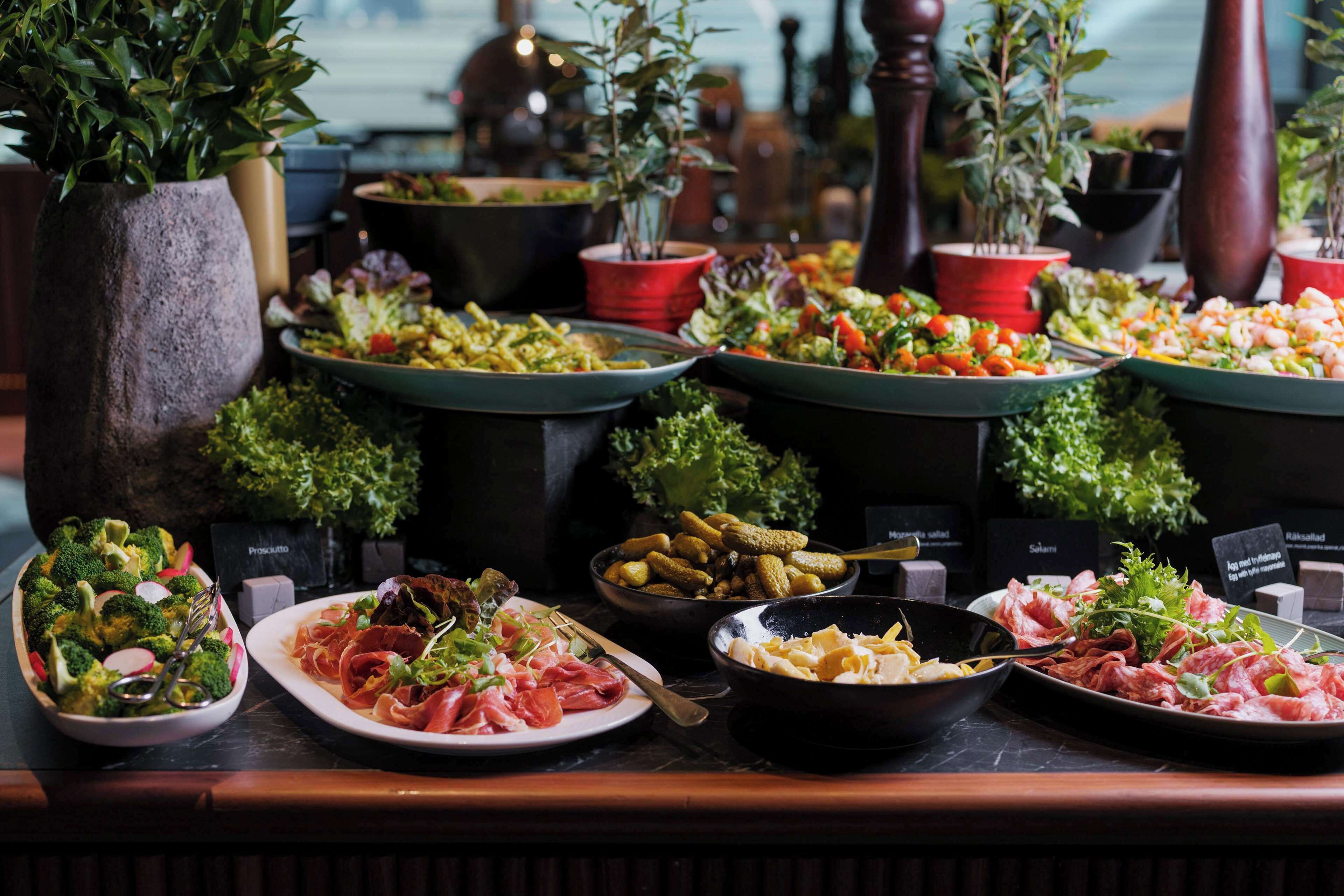 A buffet table with various dishes, including salads, meats, and vegetables, arranged on a marble countertop.