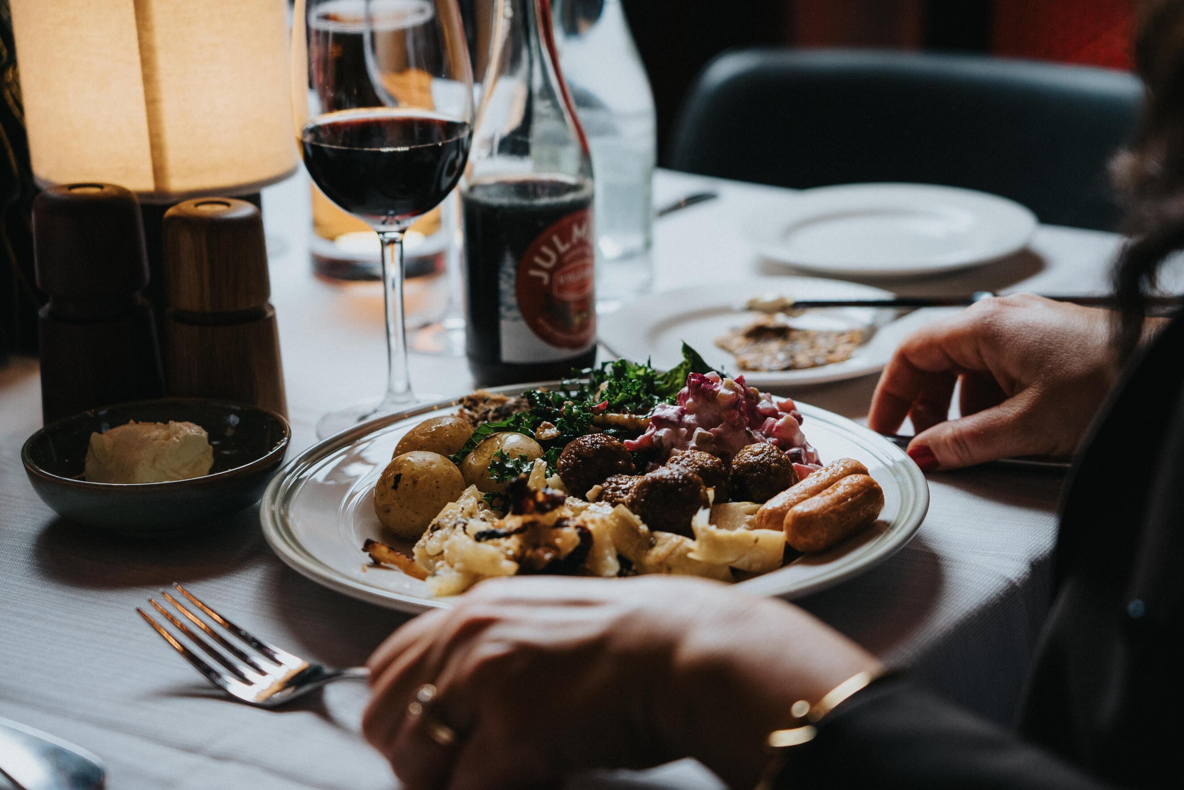 A dining table with plates of food, a bottle of Juka, a glass of red wine, and a candle.