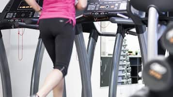 Una mujer corriendo en una cinta de correr en un gimnasio con varias cintas de correr y equipo de ejercicio.