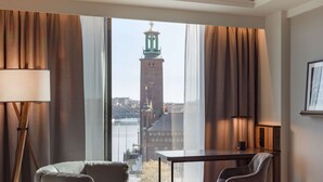 Hotellihuone, jossa on suuri ikkuna, sänky, työpöytä ja kaksi tuolia.